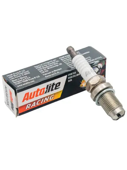 An Out of Box, Mandatory LO206 Autolite AR3910X Spark Plug Lays on the Black, White, and Orange Box it Comes in